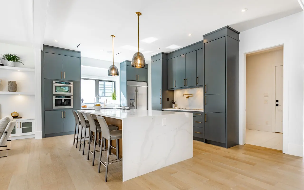Open kitchen with slate blue cabinetry, a marble waterfall island and brass pendant lights